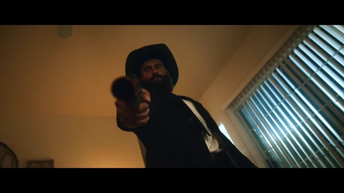 A bearded man in a black hat aiming a revolver